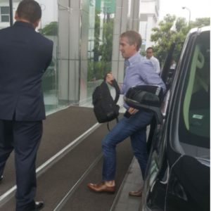 A smartly dressed driver directs his passenger into a foyer